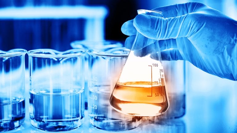Flask in scientist hand with lab glassware background in laborat