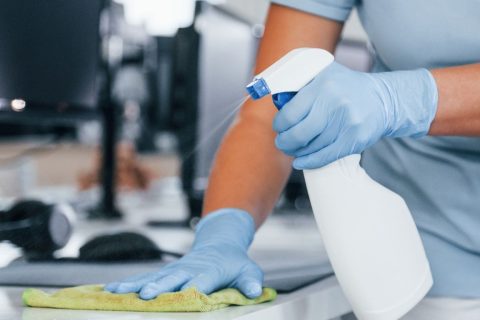 Close up view of woman in protective gloves that cleaning tables in the office.